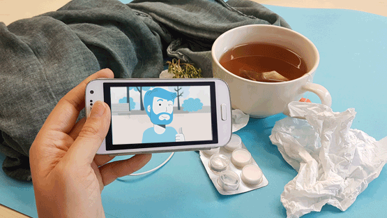 Hand mit Smartphone und Gesundheitsvideo vor Teetasse und Taschentüchern